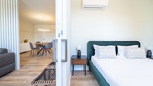 Una habitación de hotel moderna con cama, mesitas de noche, un banco, zona de comedor y equipo de aire acondicionado.