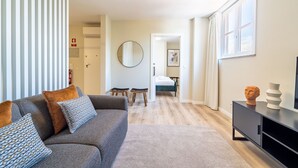 Una sala moderna con un sofá gris, dos taburetes de madera, un espejo redondo y un mueble negro con adornos.