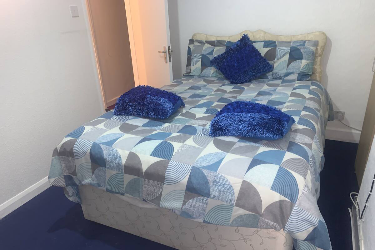 A bed with a geometric patterned bedspread and two blue pillows.