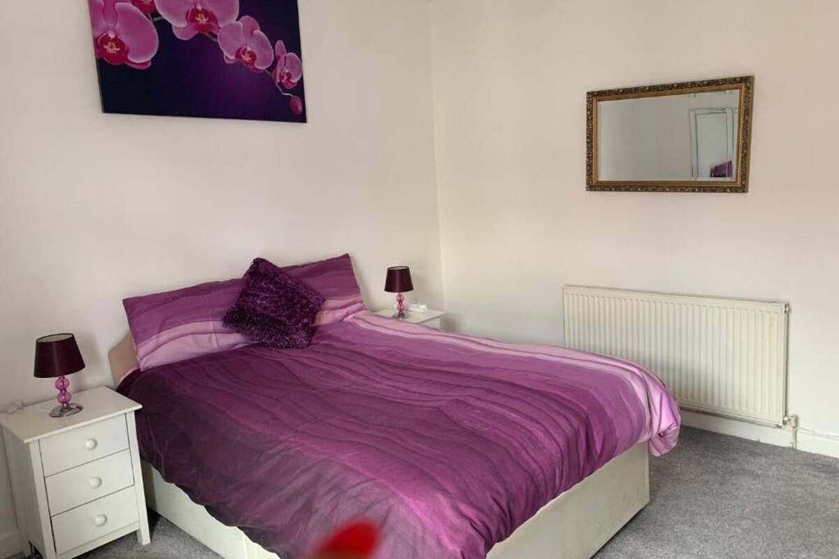 A bedroom with a bed, nightstands, a mirror, and a radiator.