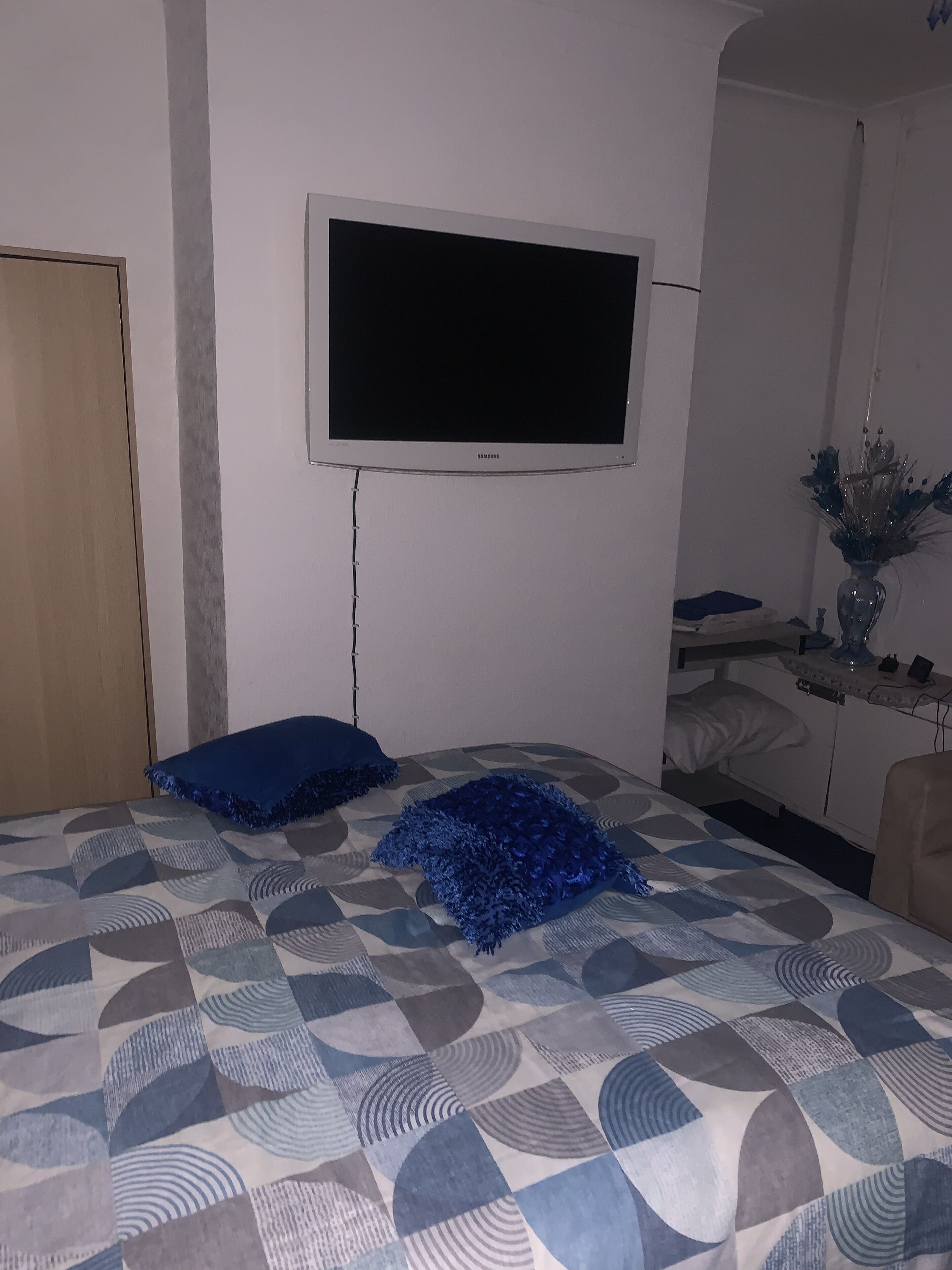 A bedroom with a bed, a TV mounted on the wall, and a bedside table with a vase.