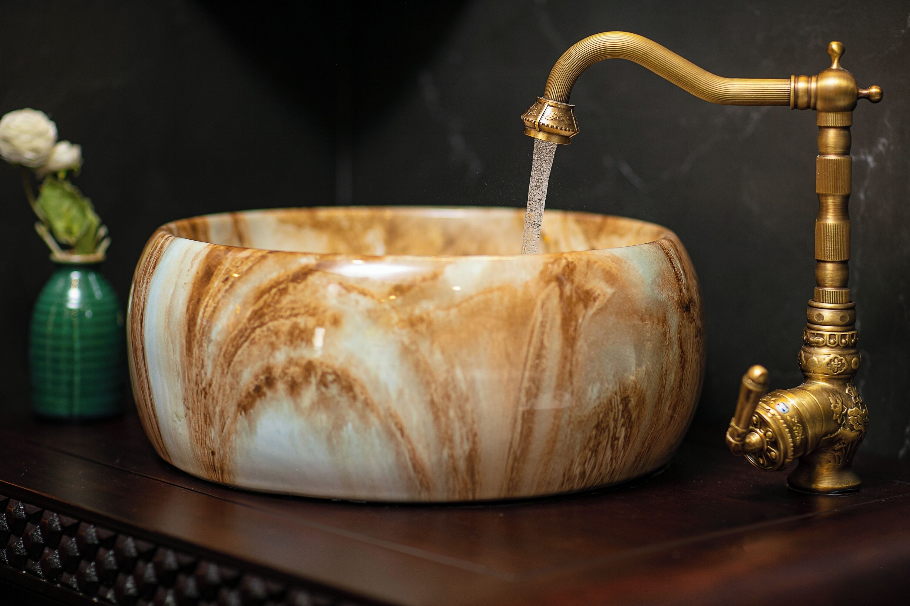 A marble sink with a brass faucet and a green vase with flowers.