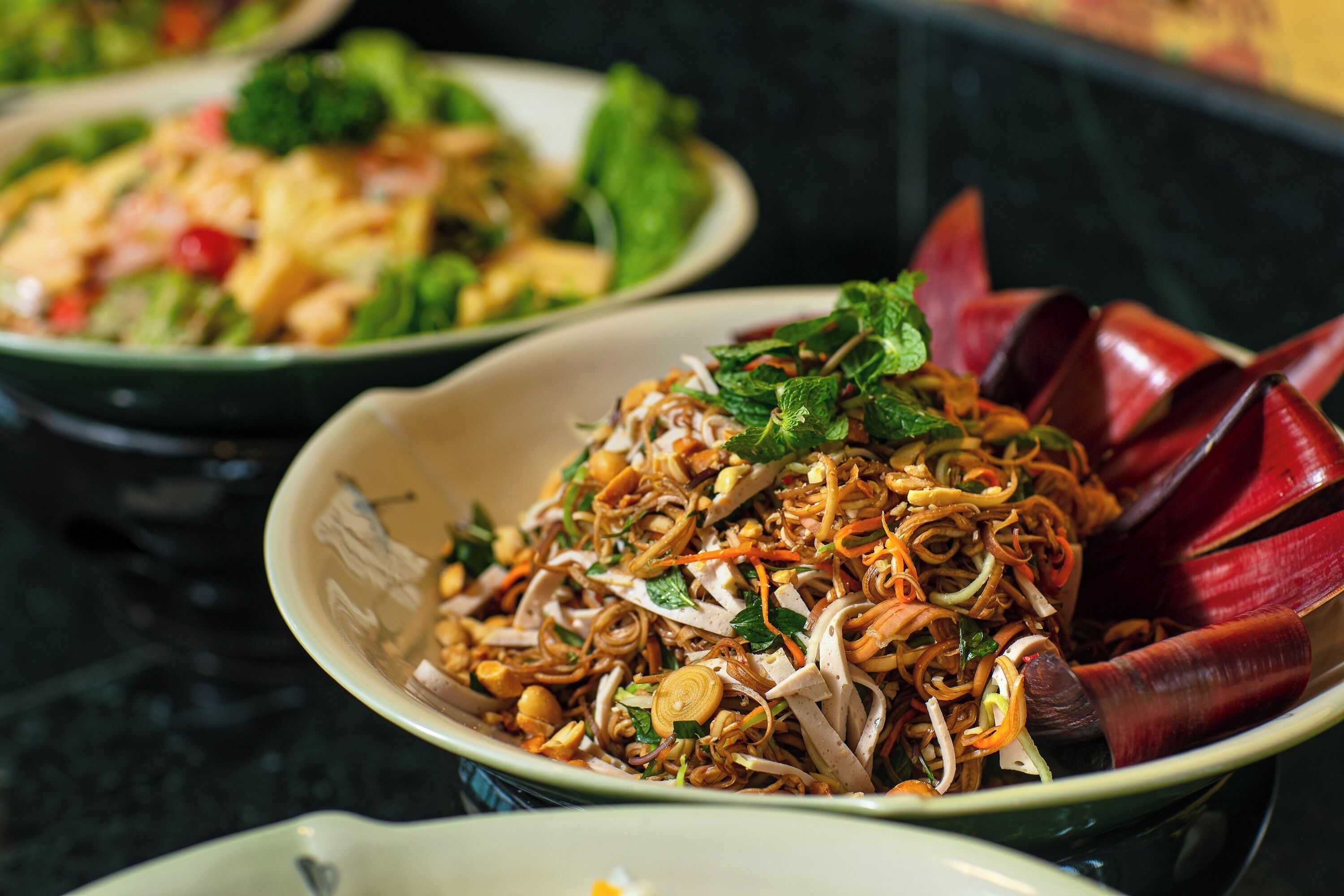 A bowl of noodles garnished with herbs and vegetables.