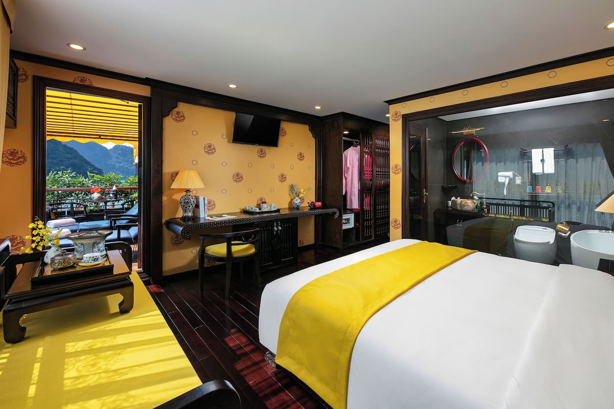 A hotel room with a bed, a desk, a chair, a table with a lamp, and a view of mountains through a window.
