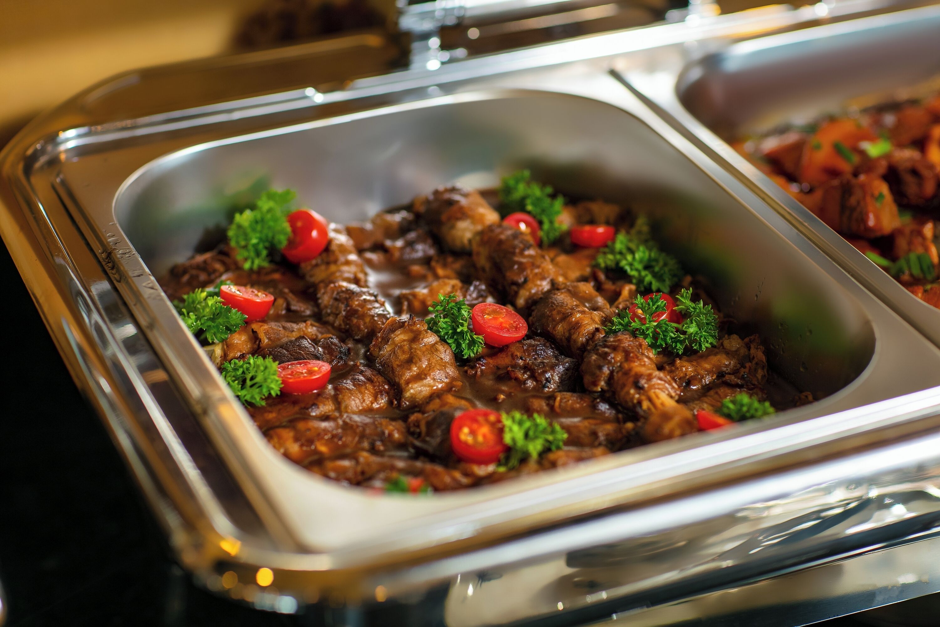 A buffet with a variety of dishes, including meat and vegetables, garnished with parsley and cherry tomatoes.