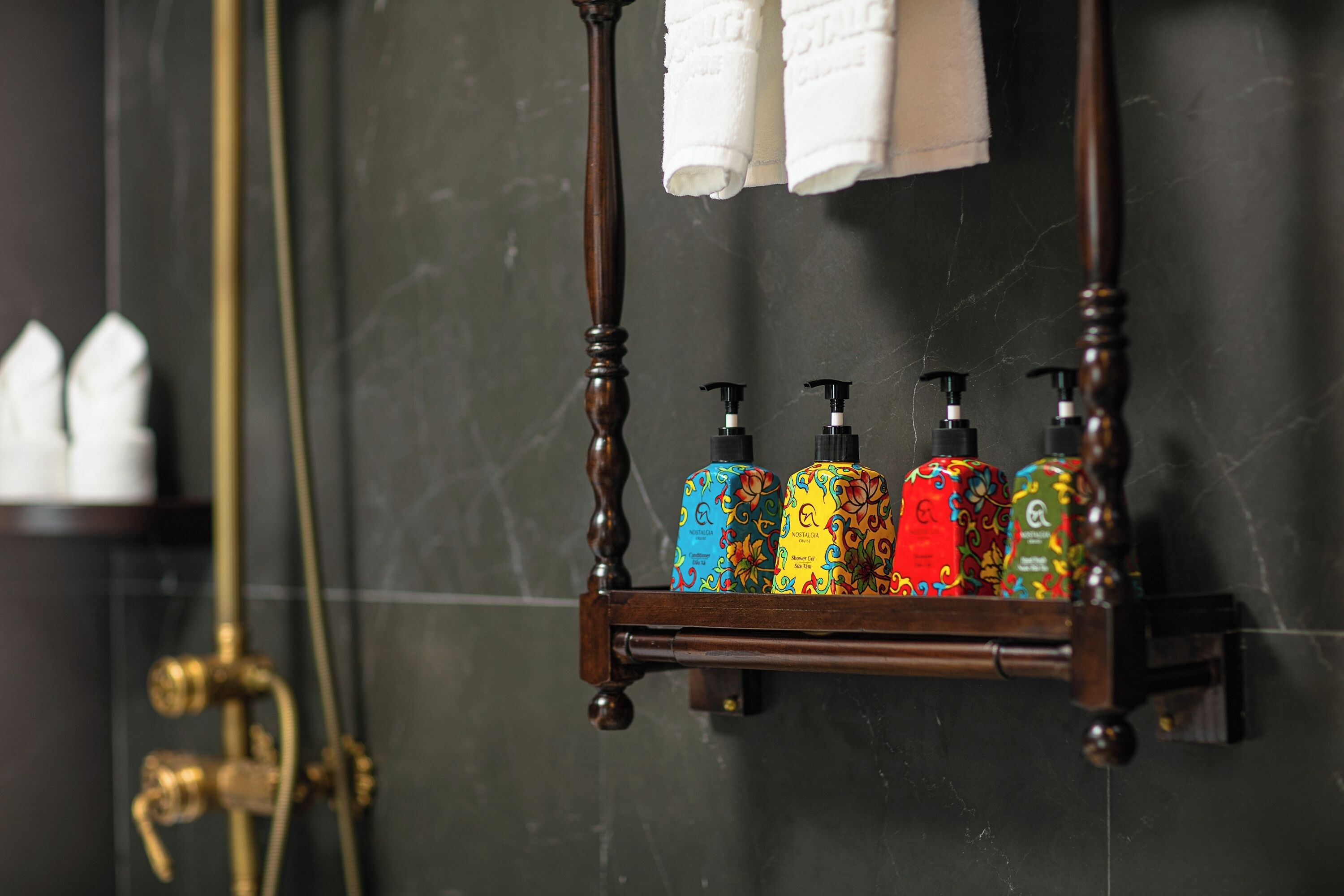 A bathroom with a wooden shelf holding colorful toiletry bottles and white towels hanging above.