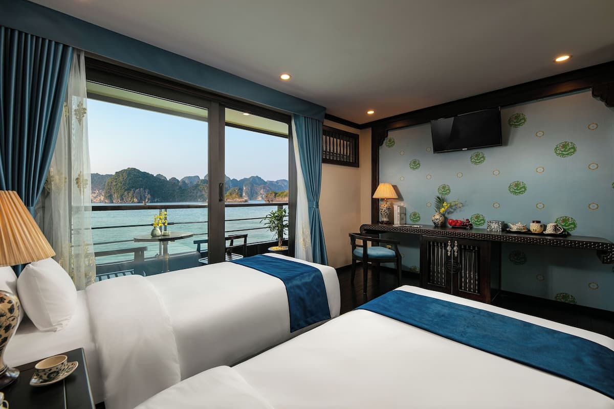 A hotel room with two beds, a desk, a TV, and a view of the sea.