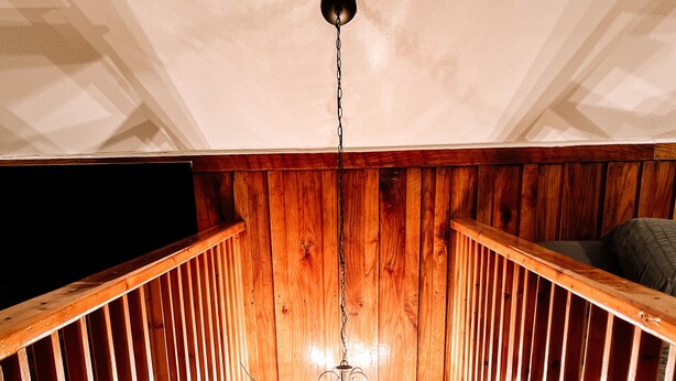 A wooden staircase with a chandelier, leading to a landing area with a checkered floor. - Muskie-Lounge River Retreat! Secluded getaway.  (Buckhannon)