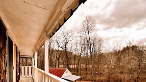 A wooden porch with a white railing, leading to a view of a rural landscape with trees and a distant building. - Muskie-Lounge River Retreat! Secluded getaway.  (Buckhannon)