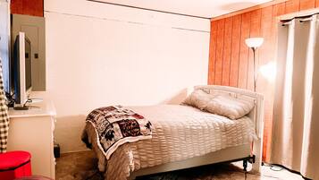 Un dormitorio con una cama, un escritorio, una silla, una lámpara y un taburete rojo.