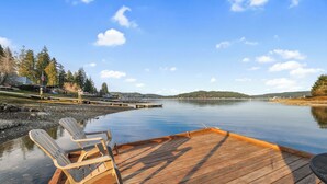 A wooden dock with two Adirondack chairs facing a calm lake, surrounded by trees and a clear sky. - Hot Tub Cabin #1 (Union)