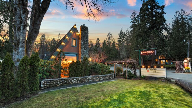 A rustic lodge with a stone chimney, surrounded by lush greenery and a clear sky. - Hot Tub Cabin #1 (Union)