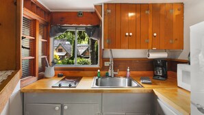 Une cuisine compacte avec des meubles en bois, un évier en acier inoxydable, une fenêtre donnant sur une maison et un four à micro-ondes.