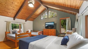 Una camera da letto con due letti in legno, una cassettiera, una televisione e ampie finestre con tende.