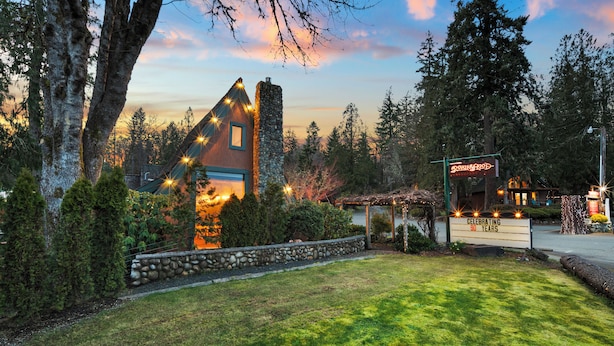 A rustic lodge with a stone chimney, surrounded by lush greenery and a clear sky. - Cabin #5 (Union)