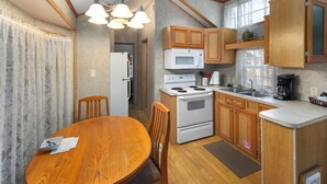 Una cocina con armarios de madera, una estufa, un microondas y una mesa de comedor con sillas.