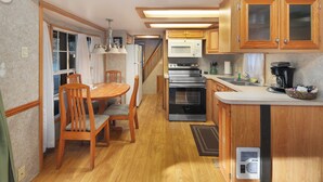 A compact kitchen with wooden cabinets, a microwave, an oven, and a dining area with chairs and a table. - Hot Tub Cabin #8 with Fire Pit (Union)