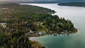 An aerial view of a lakeside property with a dock, boats, and a small settlement surrounded by dense forest and mountains in the background. - Hot Tub Cabin #8 with Fire Pit (Union)
