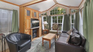 A spacious living room with a fireplace, leather sofas, a wooden coffee table, and large windows offering a view of the outdoors. - Hot Tub Cabin #8 with Fire Pit (Union)