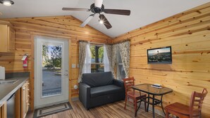 A cozy room with wooden walls, a ceiling fan, a sofa, a dining table with chairs, and a view of the outside. - Hot Tub Cabin #9 (Union)