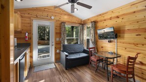 Ein gemütliches Blockhaus mit Küchenzeile, einer Sitzecke, einem Esstisch mit Stühlen und einem Deckenventilator.