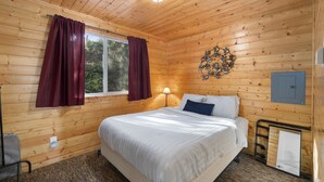 Une chambre à coucher aux murs lambrés, avec un lit, des rideaux, une lampe fixée au mur et une petite fenêtre.