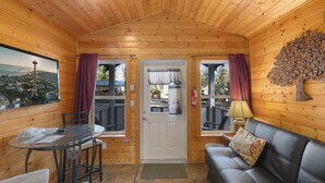 L’intérieur d’un chalet accueillant, avec une table à manger, des chaises, un canapé et une grande fenêtre agrémentée de rideaux.