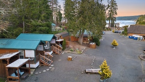 A rustic cabin area with multiple wooden structures, a gravel driveway, and a view of the water in the background. - Hot Tub Cabin #12 (Union)