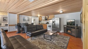 A modern living room with a leather sofa, a coffee table, and a TV. The room has wooden flooring and a kitchen area with a refrigerator and microwave. - Hot Tub Cabin #15 (Union)