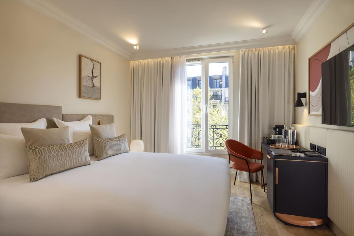 Habitación de hotel con una cama grande, un escritorio y vistas a edificios a través de la ventana.