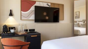 Quarto de hotel com cama, escrivaninha, cadeira, televisão e máquina de café.