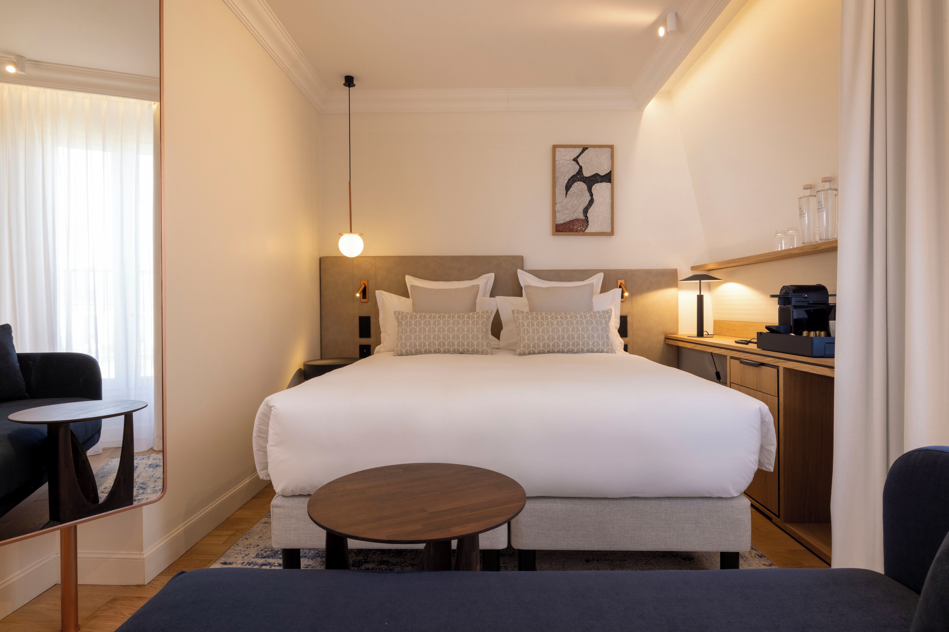 A hotel room with a large bed, a small round table, a sofa, and a desk with a lamp.