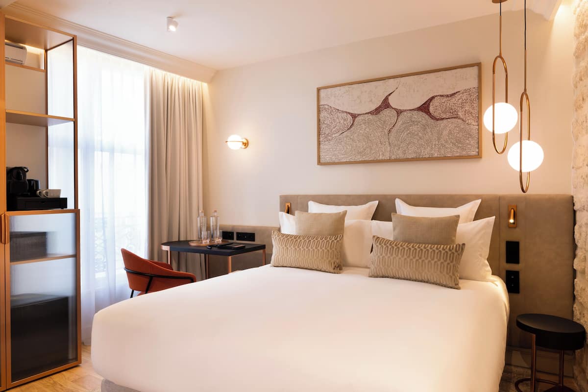 Habitación de hotel con una cama grande, un escritorio con una silla, una estantería y un cuadro en la pared.