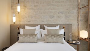 A neatly made bed with two pillows, a bedside table with a lamp, and a wall with a stone pattern. - Alberte Hotel (Paris)