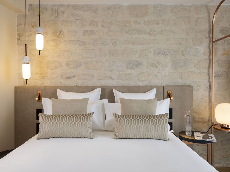Un lit bien fait avec deux oreillers, une table de chevet avec une lampe et un mur orné d’un motif en pierre.