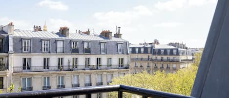 A row of multi-story buildings with balconies, a clear sky, and some greenery.