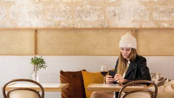 Una persona sentada a una mesa con una bebida, en una habitación con paredes de piedra y un separador tejido.