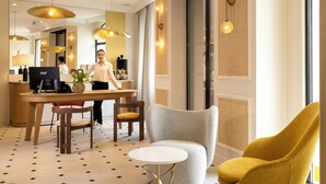 A modern hotel lobby with a reception desk, a seating area with a round table and chairs, and a large window providing natural light. - Alberte Hotel (Paris)
