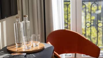 Een tafel met twee flessen, drie glaasjes, een afstandsbediening en een stoel met uitzicht op een balkon.