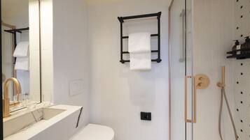 A bathroom with a white sink, a toilet, a glass shower enclosure, and a towel rack.