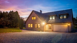 A two-story house with a garage, a driveway, and a well-maintained lawn. - Opulent, relaxing home with hot tub (Fochabers)
