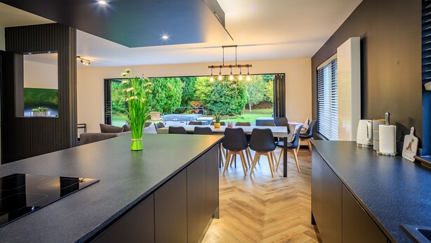 A modern kitchen with a large island, built-in appliances, and a dining area with a view of the garden. - Opulent, relaxing home with hot tub (Fochabers)