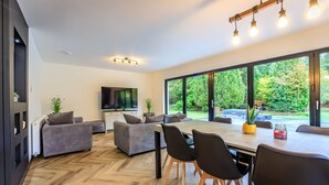 A modern living room with a dining area, large windows, and a flat-screen TV. - Opulent, relaxing home with hot tub (Fochabers)