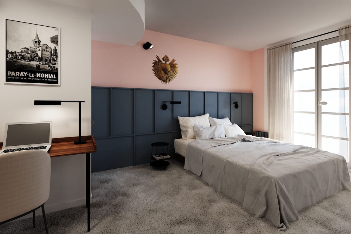 A bedroom with a bed, a desk with a laptop, a wall-mounted light, and a poster.