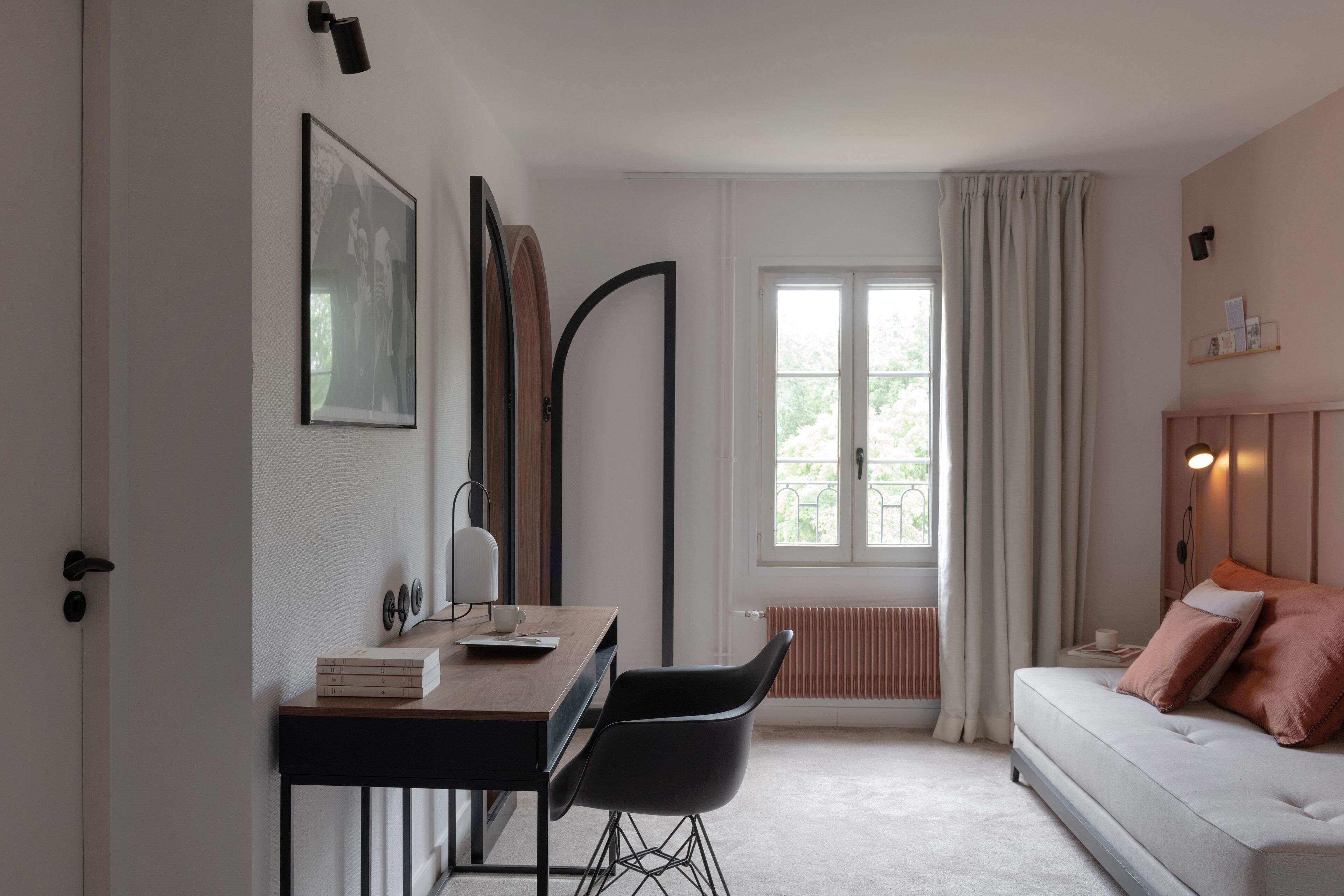 A modern bedroom with a bed, a desk with a chair, a window with curtains, and a radiator.