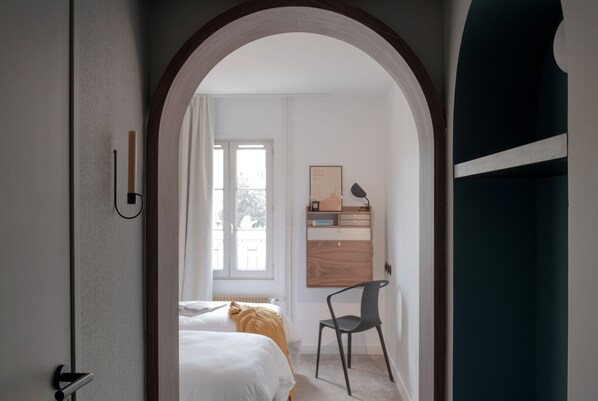 A hotel room with a bed, a chair, a desk, and a window.