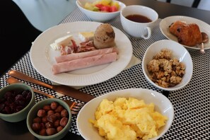 Una mesa de desayuno con platos de comida, tazones de nueces y fruta, y una taza de café.