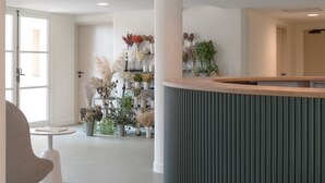 Una zona de recepción moderna con un mostrador curvo, un área de descanso con una silla y una exhibición de plantas.