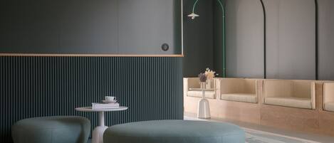 Un espacio lounge moderno con una pared verde oscuro, un sofá beige y dos zonas de estar circulares.
