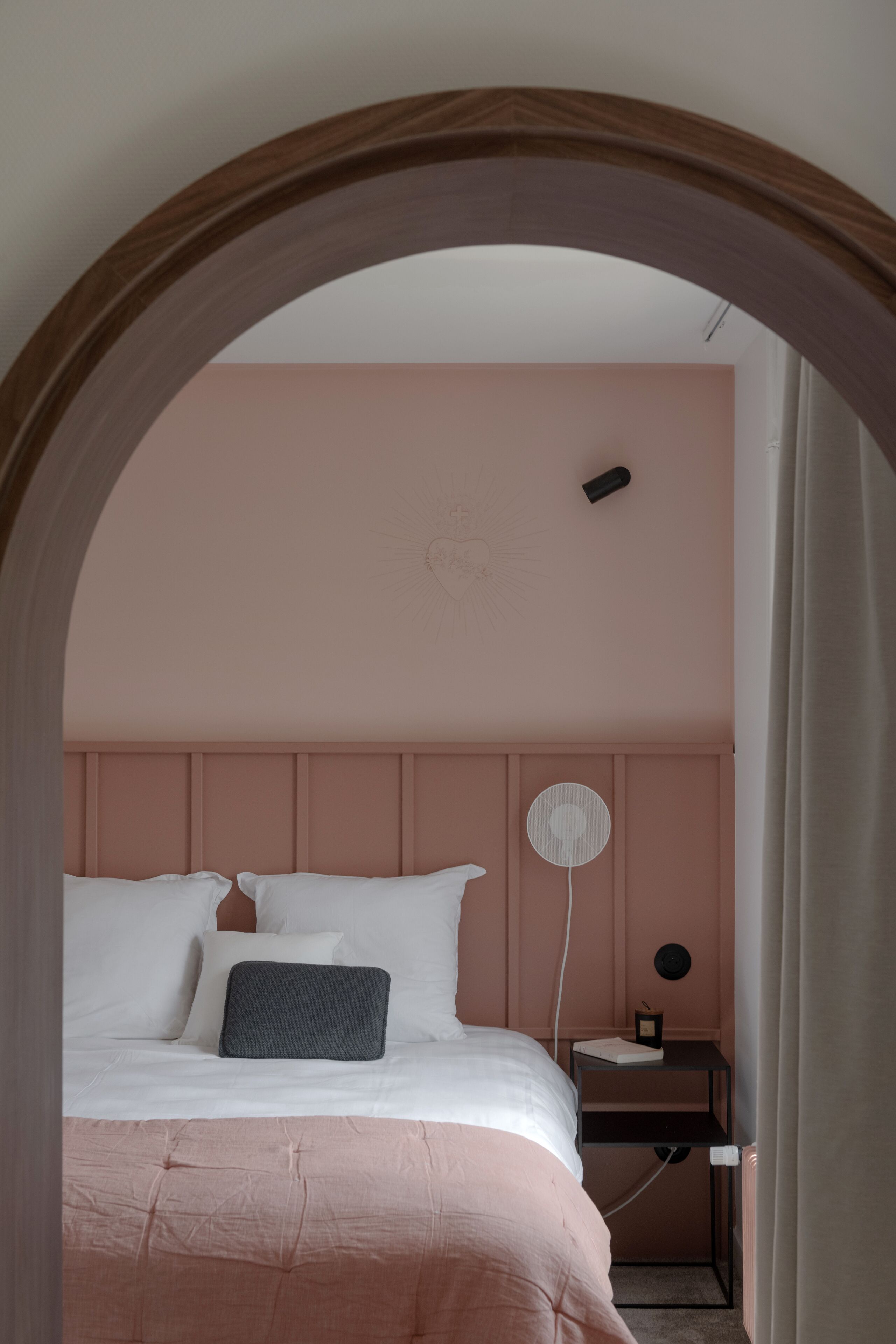 Un dormitorio con cama, mesita de noche y un ventilador de pared.